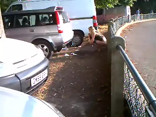 Woman pissing in public beyond some cars